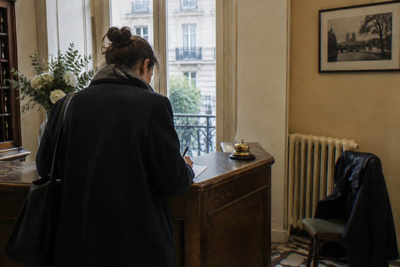 Reception desk of a small Paris hotel with a guest signing a paper form