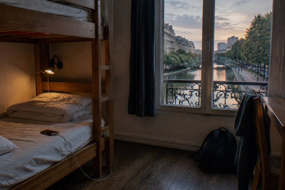 A wooden bunk bed frame with a folded duvet and a personal reading light in a quiet dorm room