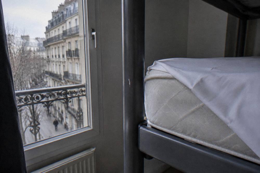 A close view of a mattress corner with tight white sheets folded back on a hostel bed