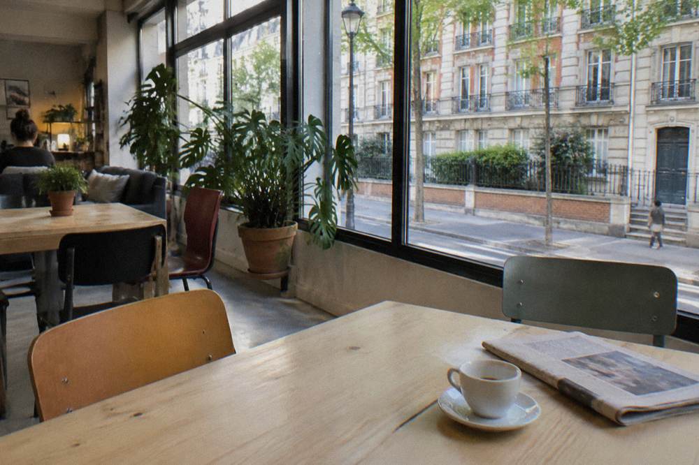 A bright modern hostel common room with wooden tables and large windows onto a Paris street