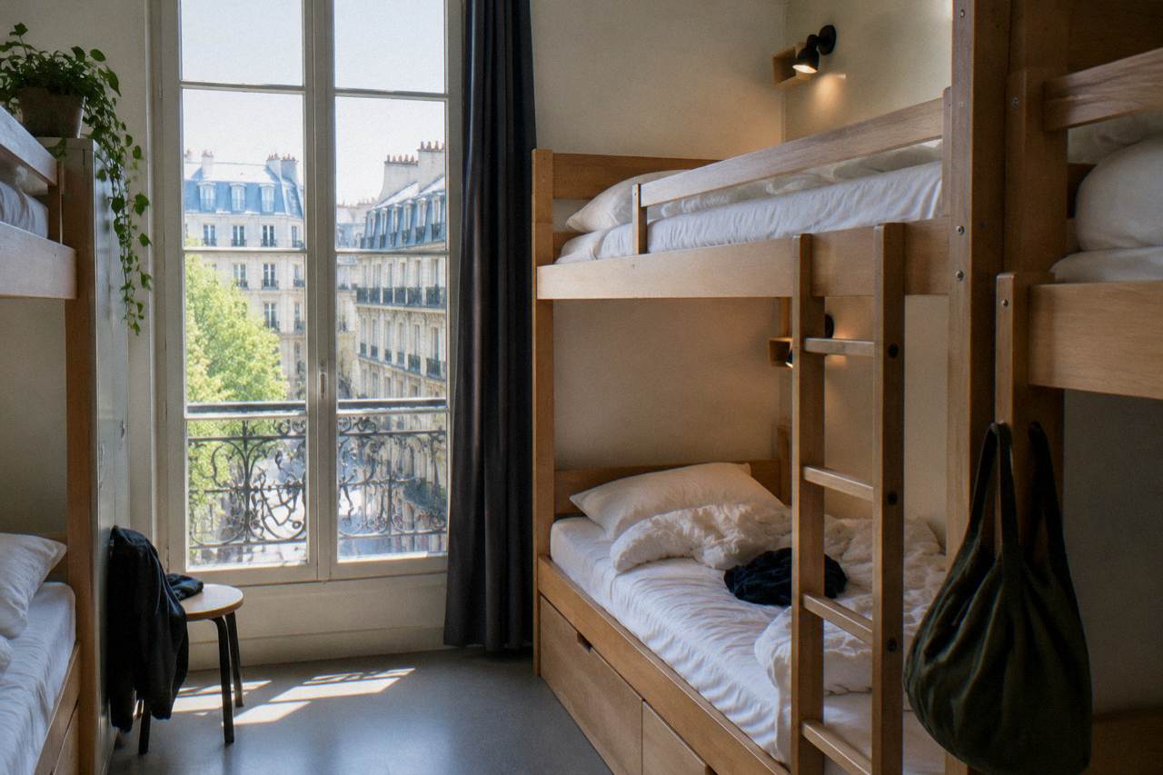 A row of neatly made bunk beds with individual reading lights in a bright Paris hostel dorm room
