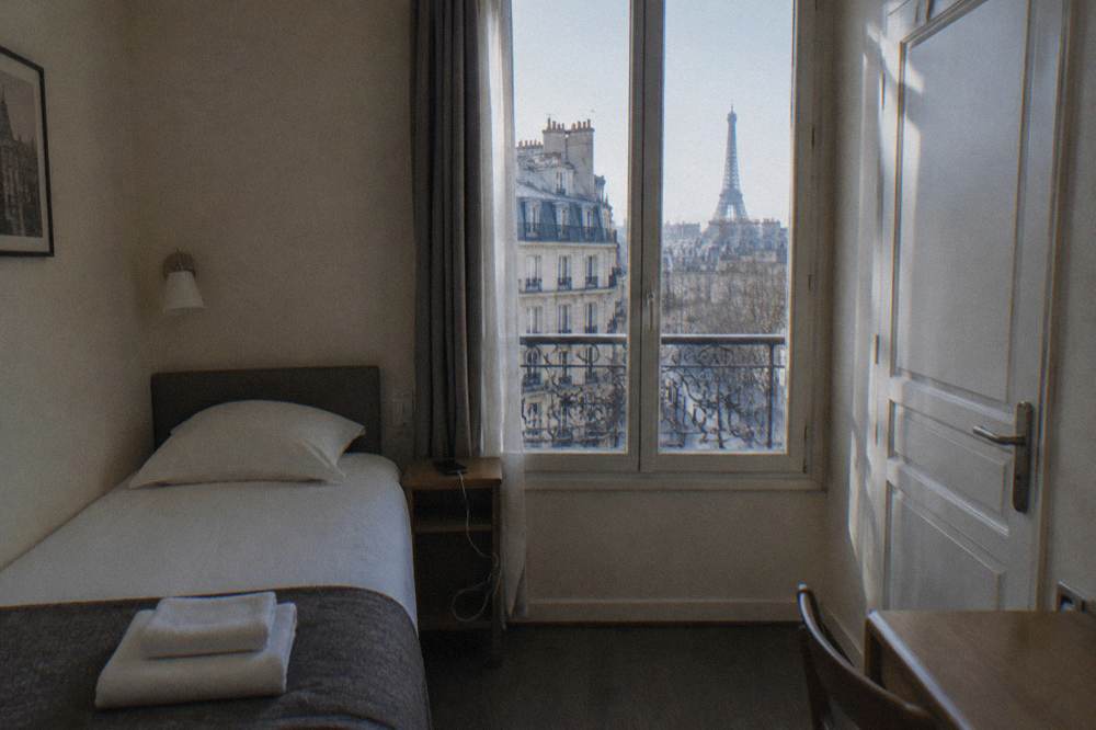 A single bed with folded towels in a small simply furnished Paris hotel room