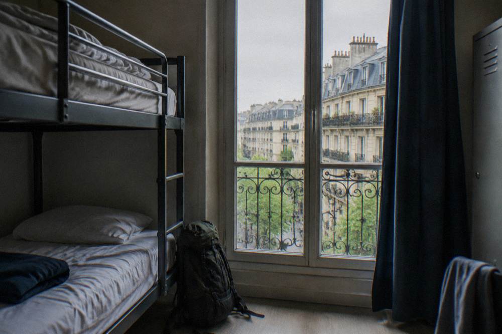 Bunk beds in a bright hostel dorm room with a window onto a Paris street