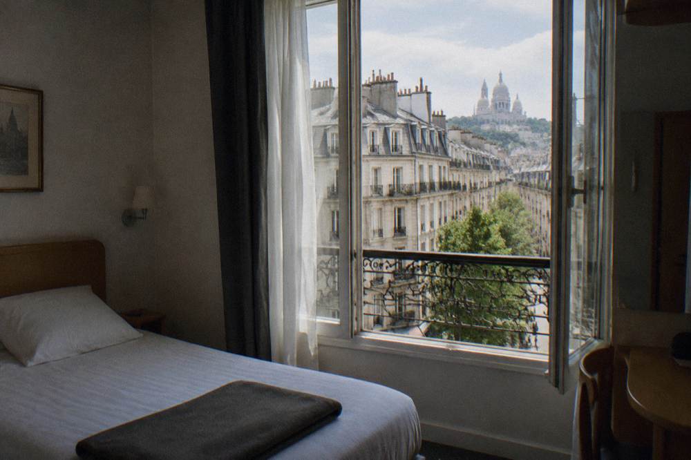 A simple hotel room in Paris with a made bed and a window onto the street