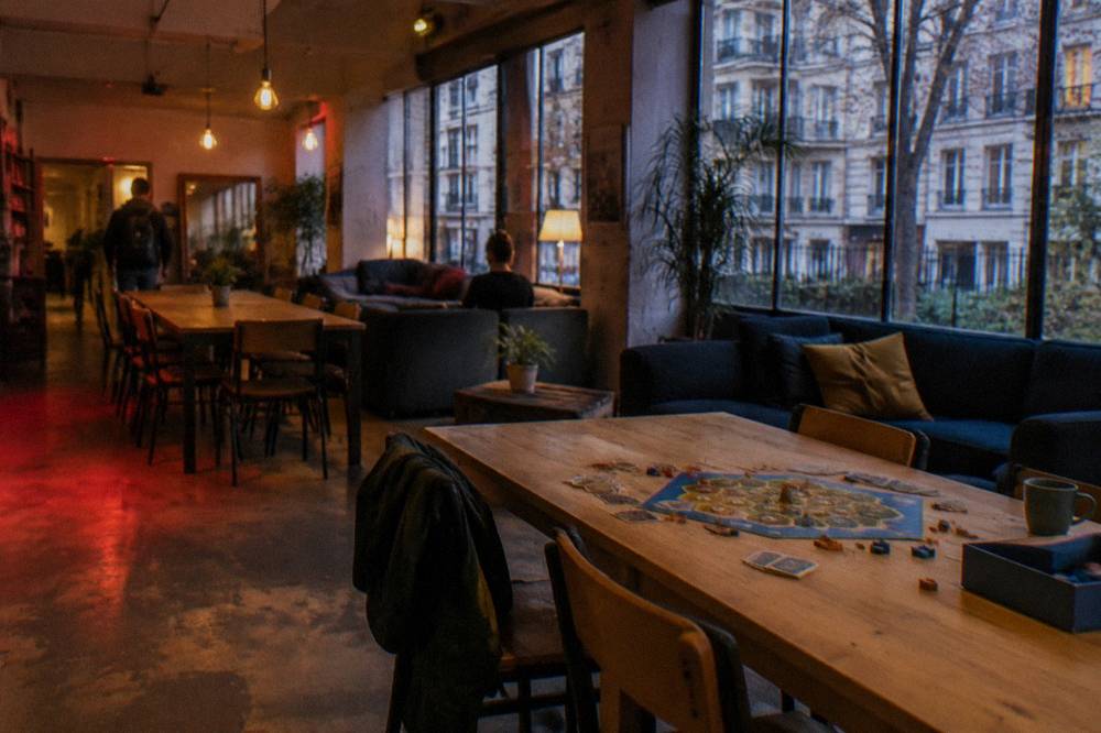 A communal hostel lounge with long wooden tables, sofas and warm lighting