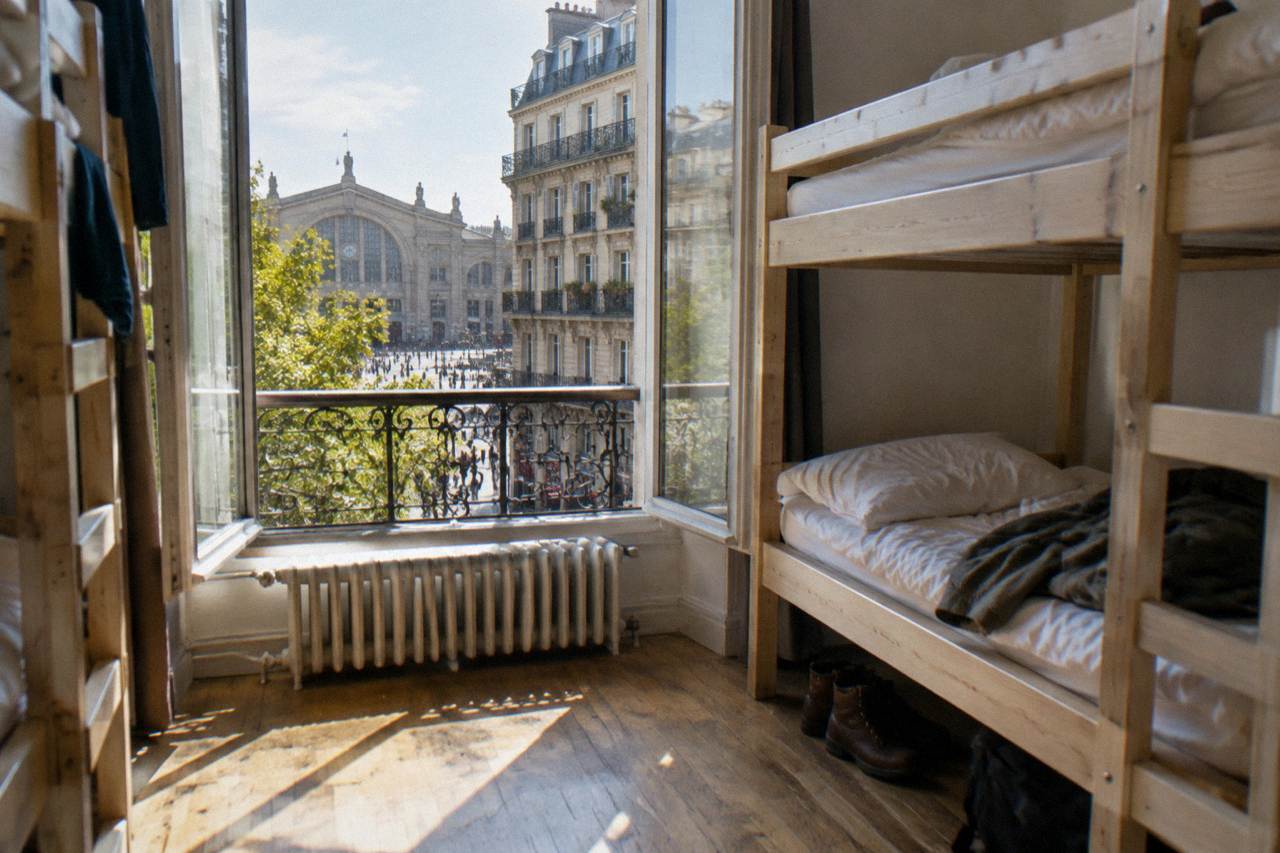 Bunk beds in a bright Paris hostel dorm room with wooden frames and a window onto a street