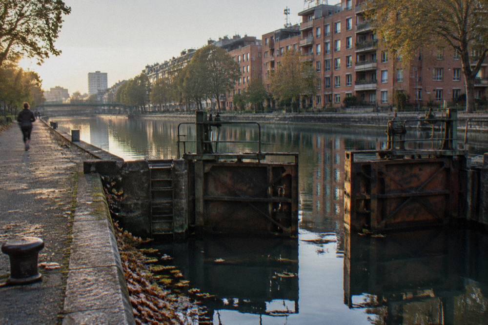 A canal-side Paris street in the morning with apartment buildings along the water
