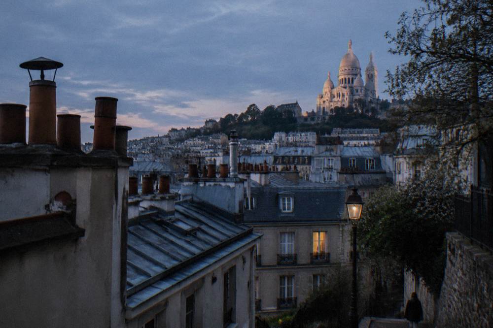 Paris rooftops at dusk with chimney pots and distant hill