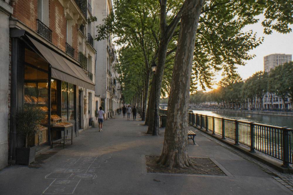 A tree-lined Paris street in a residential neighbourhood with a bakery awning and parked bicycles