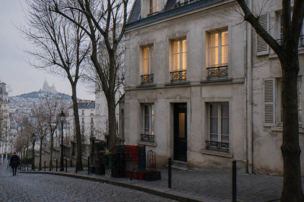 Small Paris hotel facade with lit windows on a sloping cobblestone street