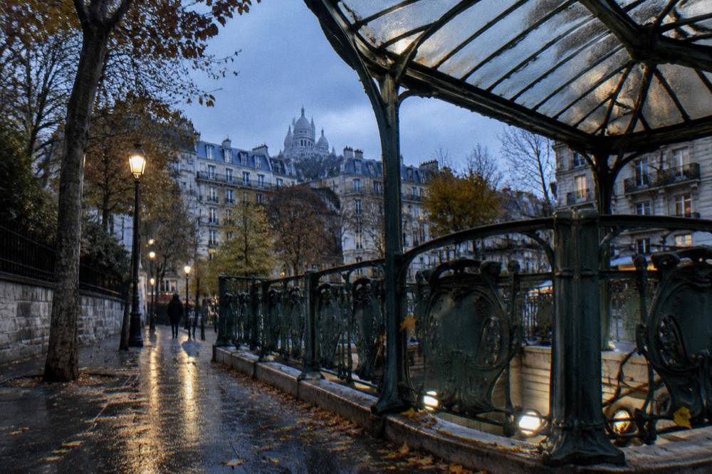 Paris metro station entrance with green railings and signage on an evening street
