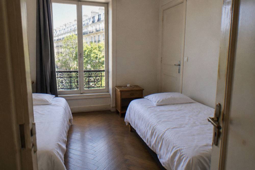 A simple private guest room with twin beds, a nightstand and a closed interior door