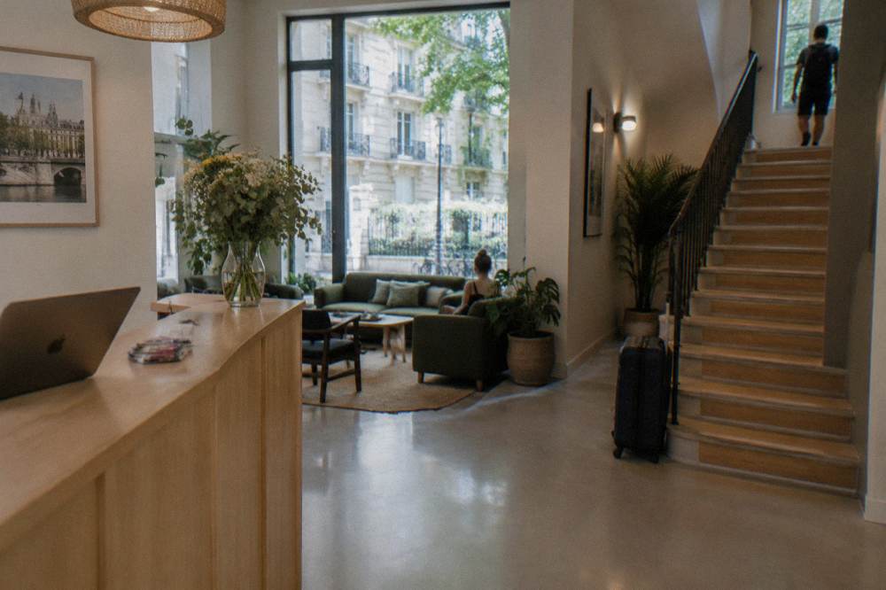 A hostel reception area with a wooden counter, seating and a staircase to guest floors