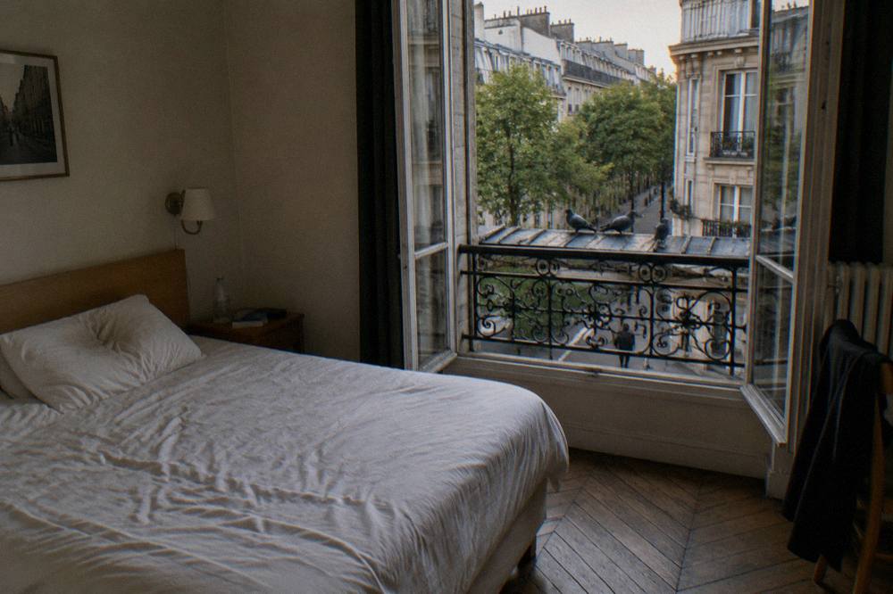 A small Paris hotel room with a double bed, wooden floors and a window onto the street