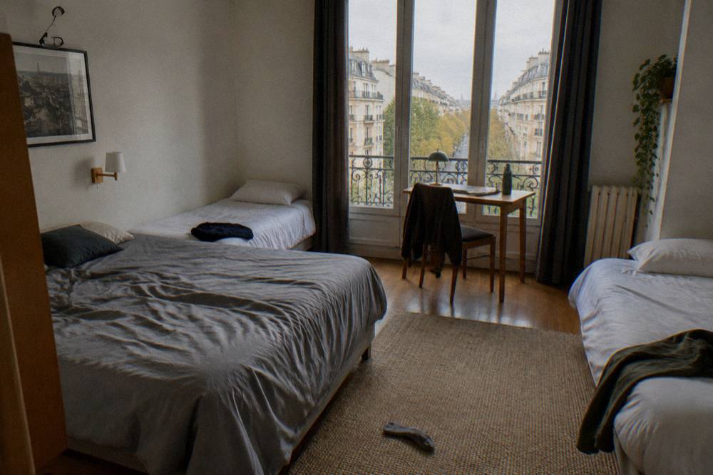 A family-sized hotel room with a double bed, two single beds and a small desk under a window