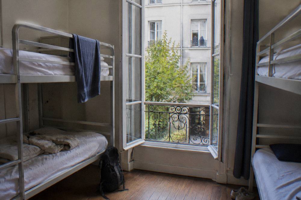Bunk beds in a bright hostel dorm room with a window onto a Paris courtyard