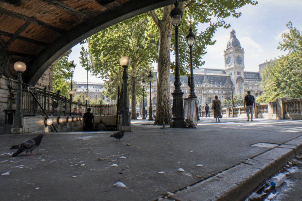 A metro station entrance on a Paris boulevard with a train viaduct behind