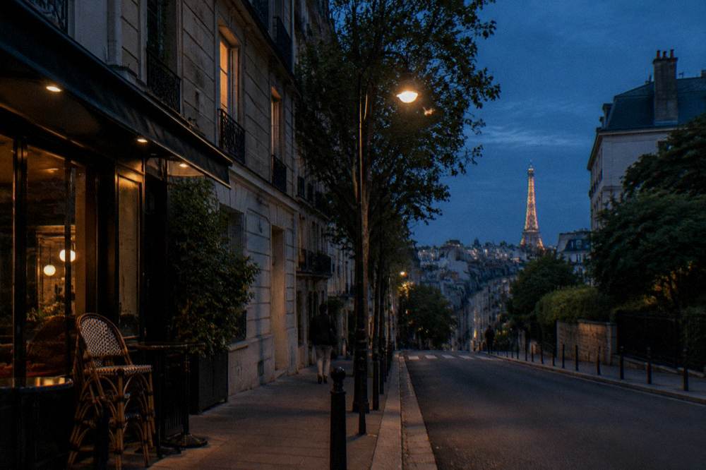 An evening view down a calm Paris street with lit windows and a distant lit monument