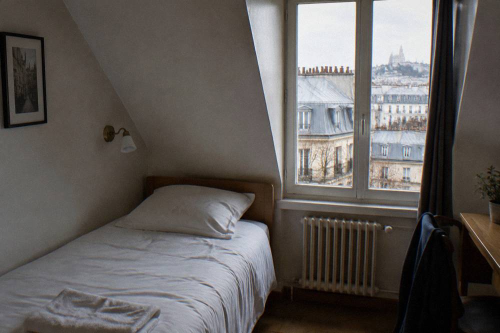 A narrow single bed under a sloped attic ceiling in a small Paris hotel room