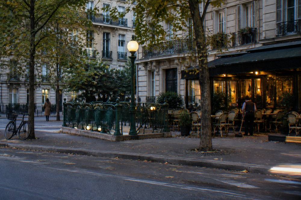 A Paris boulevard in the evening with a metro entrance glowing near small hotels