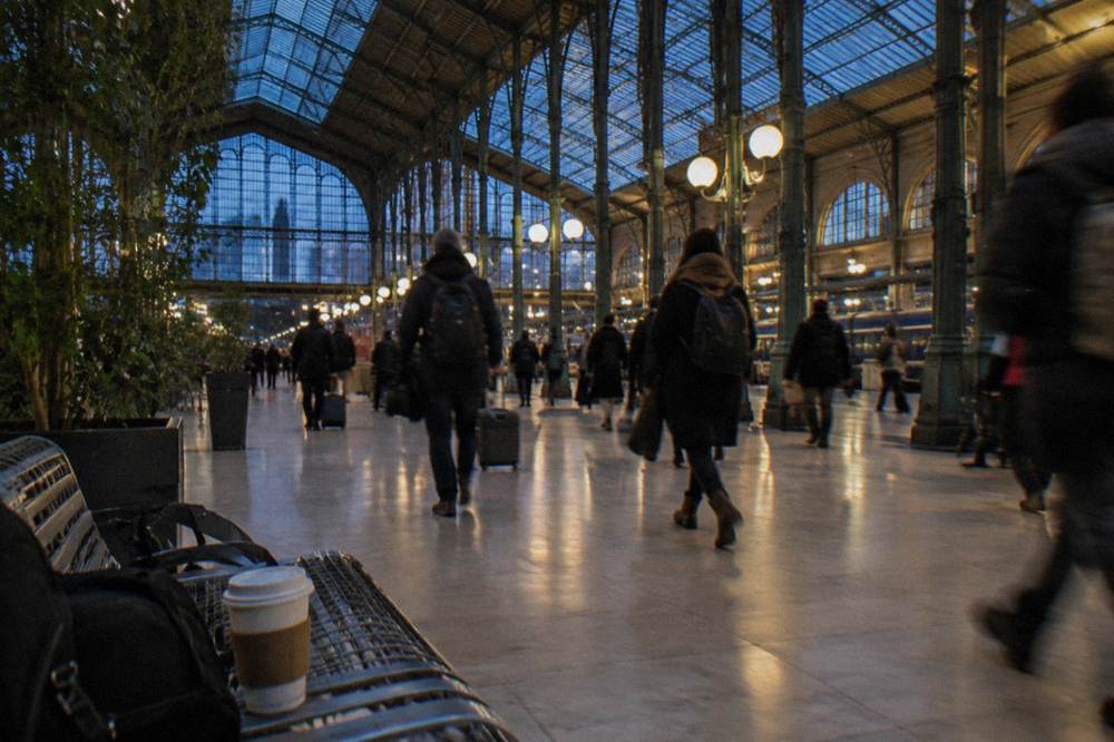 A busy Paris railway station concourse with departure boards and travellers with backpacks