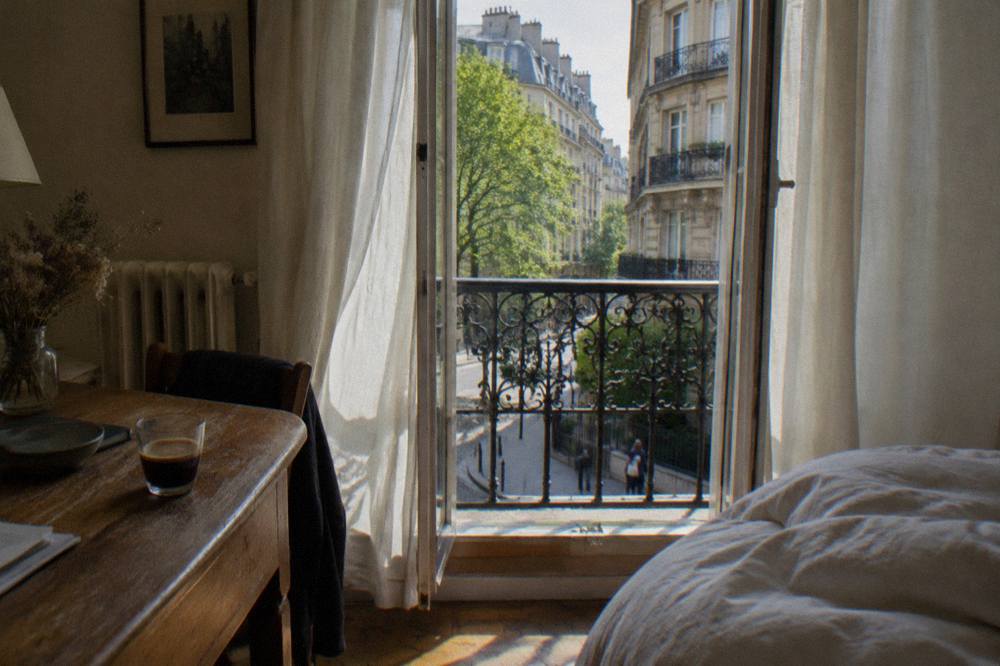A small hotel room with tall French windows letting in afternoon light