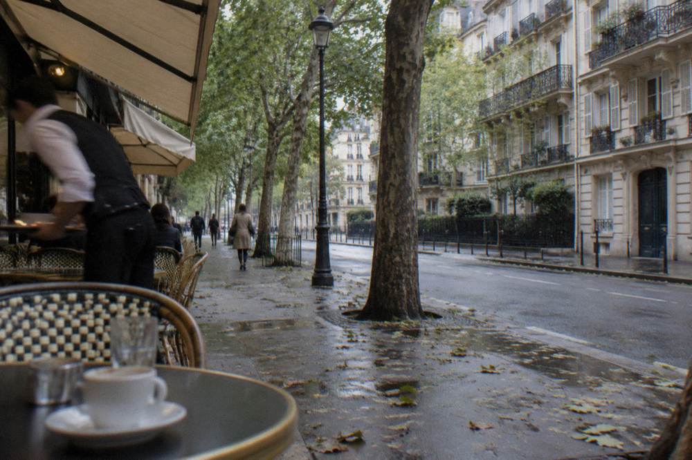 A tree-lined Paris street with cafe awnings and apartment balconies