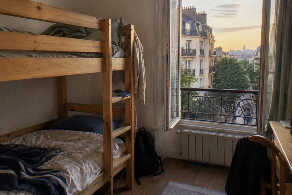 A hostel dorm room with wooden bunk beds and a window onto a street