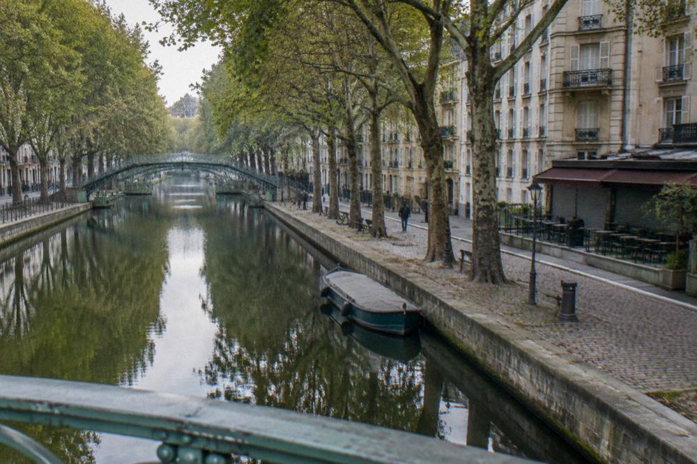 Canal-side Paris street with trees and old apartment buildings in morning light