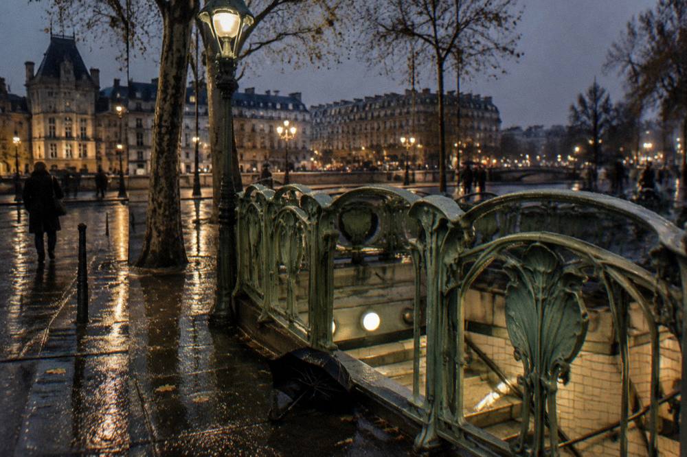 A metro station entrance on a Paris street with its classic sign and Guimard-style railings