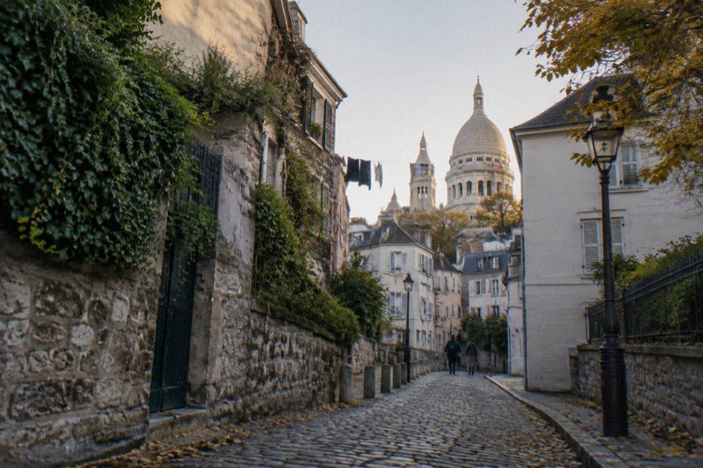 A cobblestone Paris lane rising toward a white domed basilica at the top of a hill