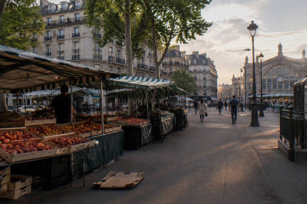 A wide Paris boulevard with market stalls and apartment blocks under a late afternoon sky