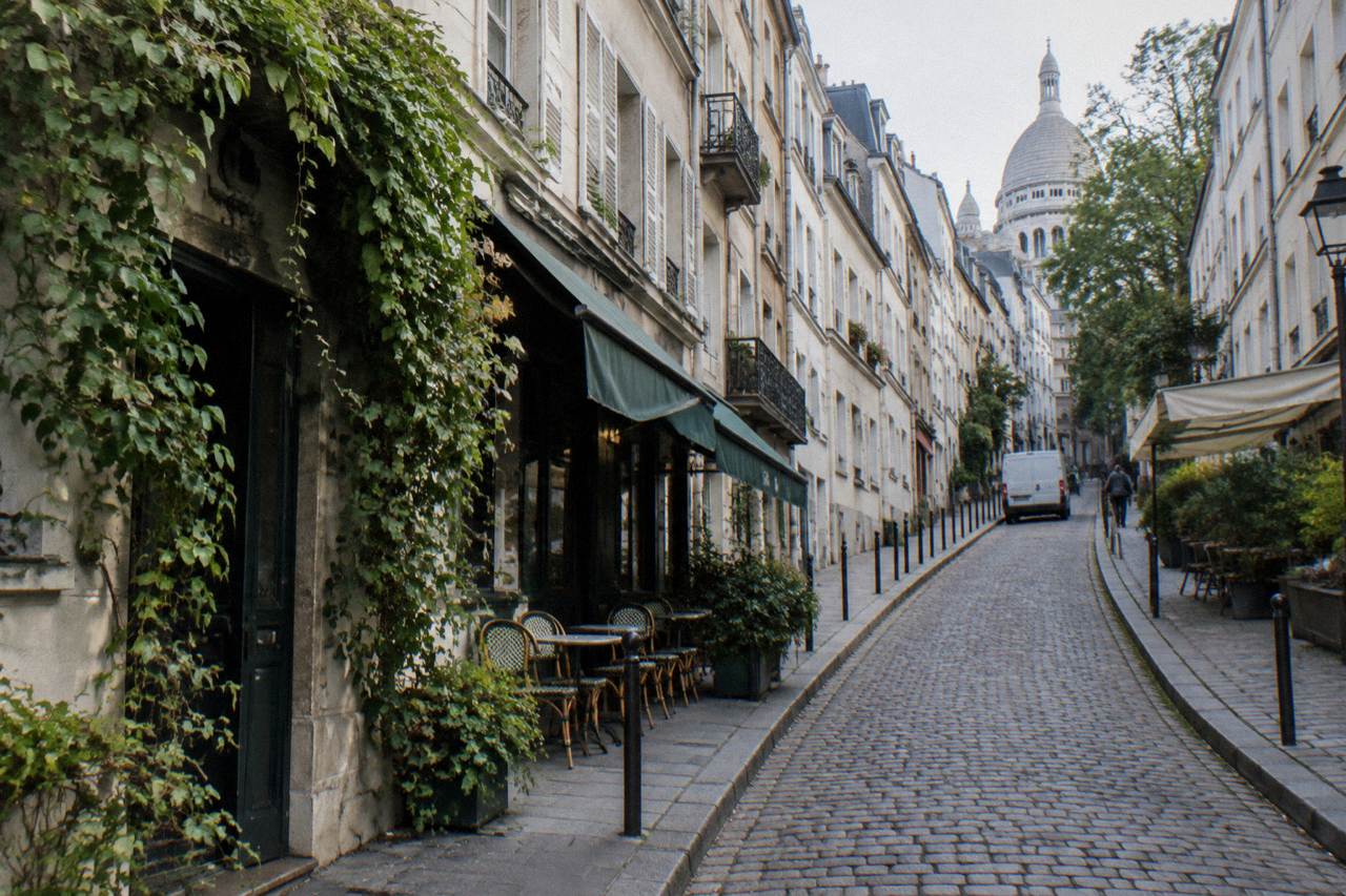 A narrow Paris street climbing a hill with pale apartment buildings and cafe awnings