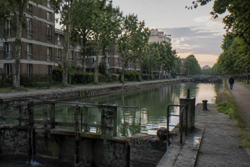 A canal-side Paris street in the 19th arrondissement with trees and low apartment blocks
