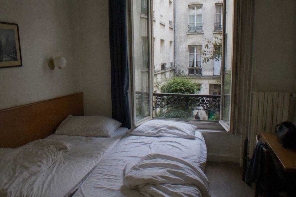 A bright budget hotel double room with two single beds pushed together and a window onto a courtyard