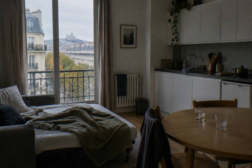 An aparthotel living area with a sofa bed, small dining table and a kitchenette along the wall