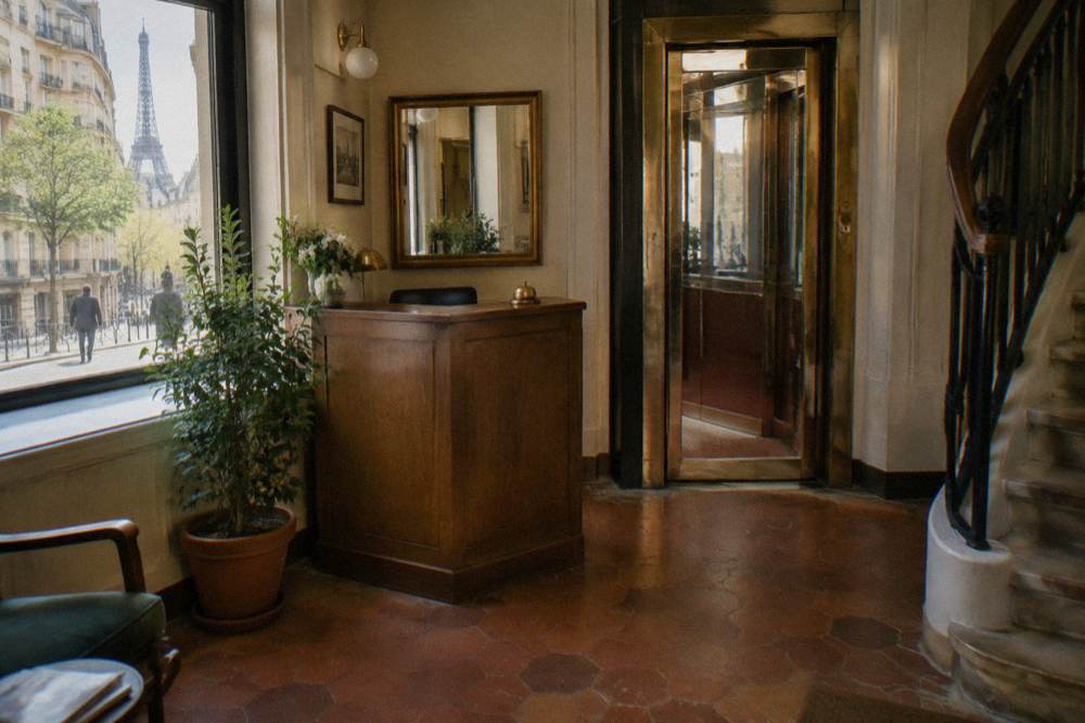 A lift lobby in a small Paris hotel with a tiled floor and a wooden reception desk