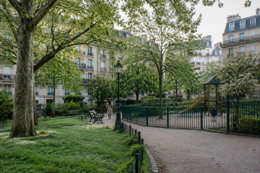 A tree-lined Paris square in a residential neighbourhood with benches and a playground fence