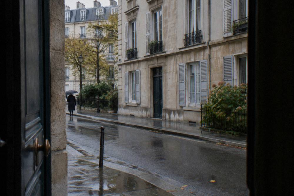 An apartment building facade in a quiet residential Paris street with shutters and narrow windows