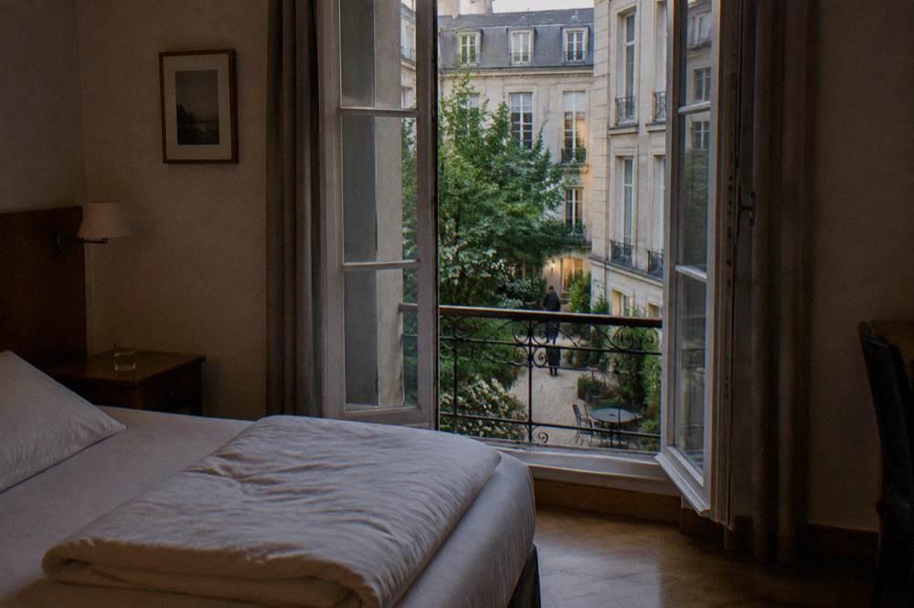 A small double hotel room in Paris with a folded duvet, bedside table and window onto a courtyard