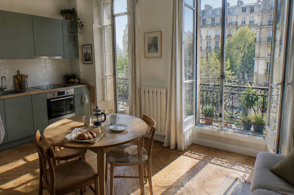 A bright Paris apartment interior with tall windows, a small kitchenette and a table set for two