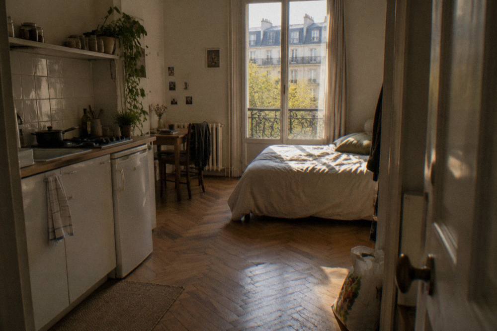 A studio room with a small kitchenette along one wall and a double bed beside a window