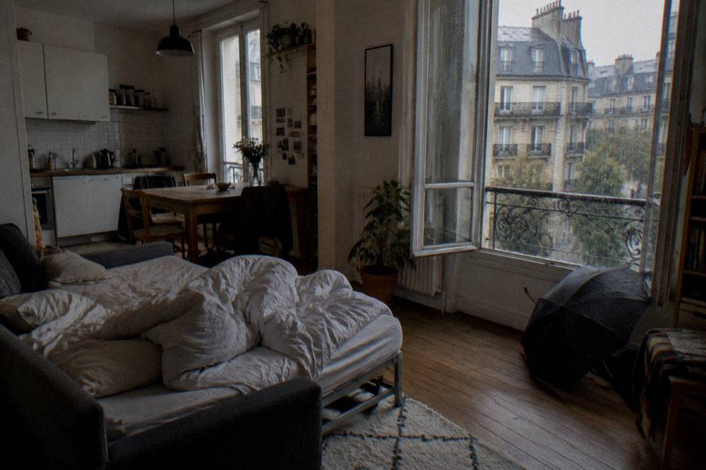 A sofa bed folded out in a Paris studio with a dining table and kitchen behind it