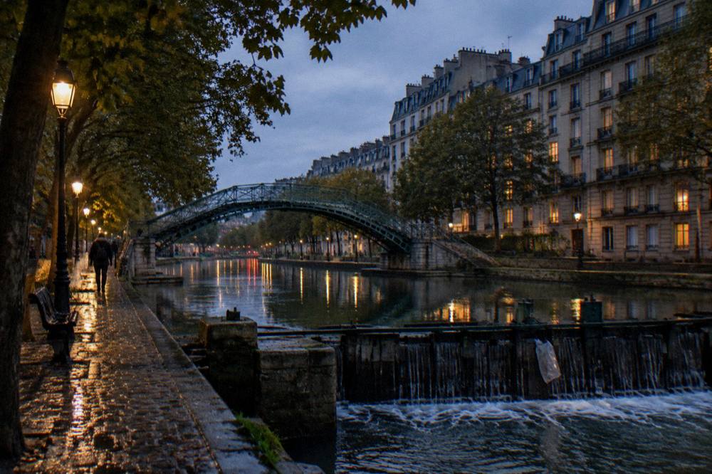 An evening view along a canal-side quay in northern Paris with apartment buildings and trees