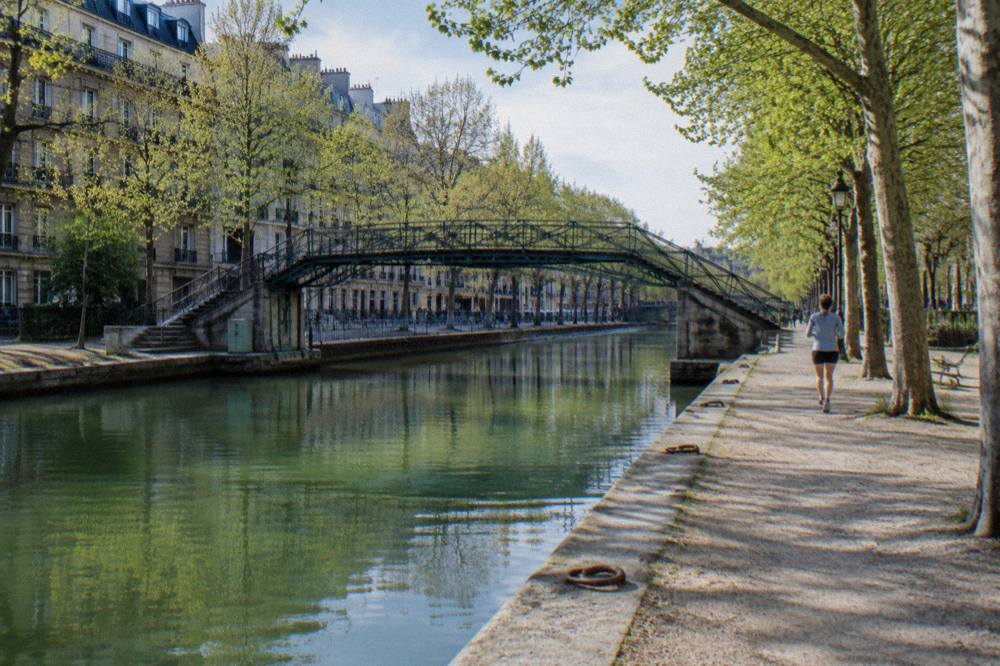 A canal path in Paris with trees along the water and a footbridge