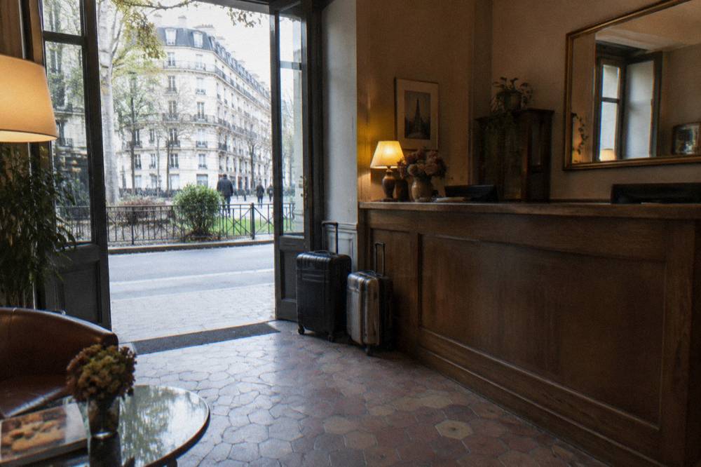 A hotel lobby with tiled floors, a small front desk and luggage beside the door