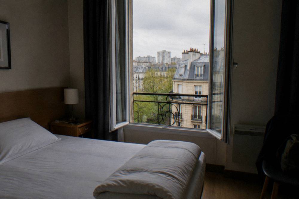 A small double hotel room in Paris with a folded duvet and a window onto the street