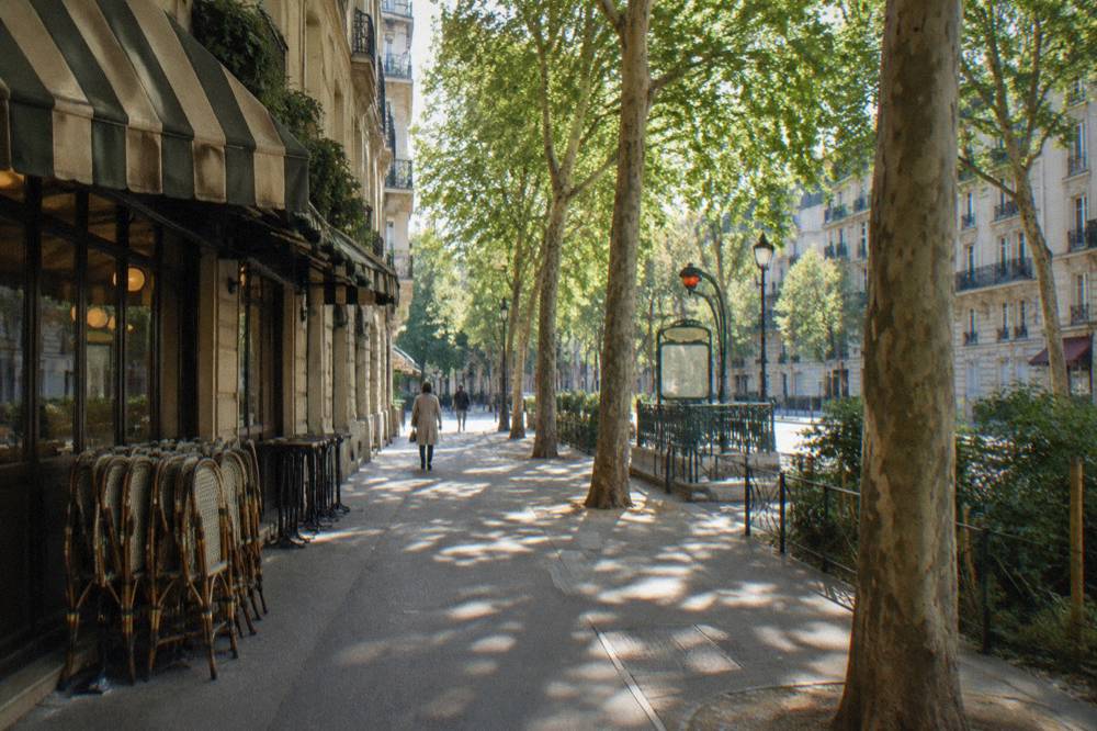 A tree-lined street in a residential Paris neighbourhood with cafe awnings and parked bicycles