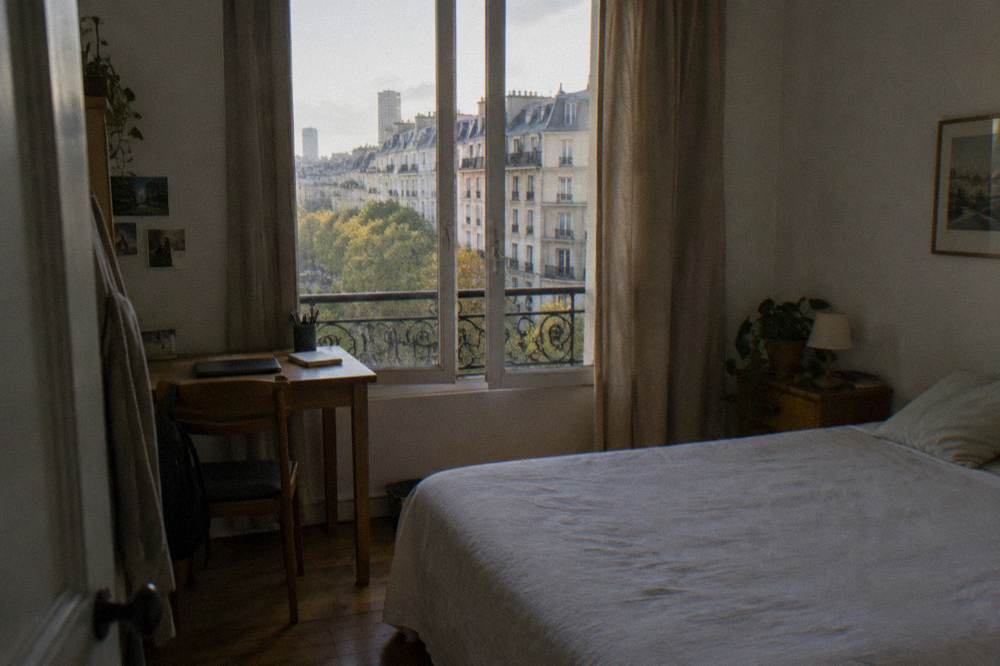 A simple double hotel room in Paris with a made bed, desk and window onto the street