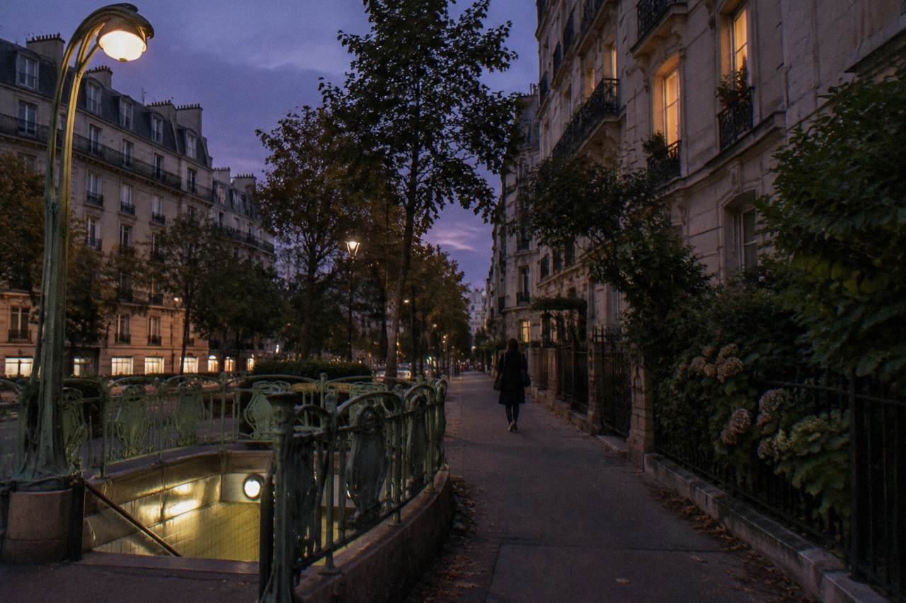 A quiet Parisian residential street at dusk with lit windows and a metro entrance